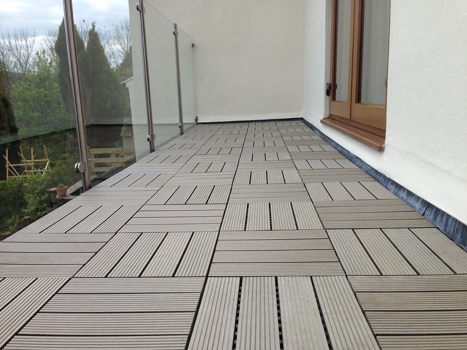 A balcony floored with timber decking tiles behind a glass and steel balustrade