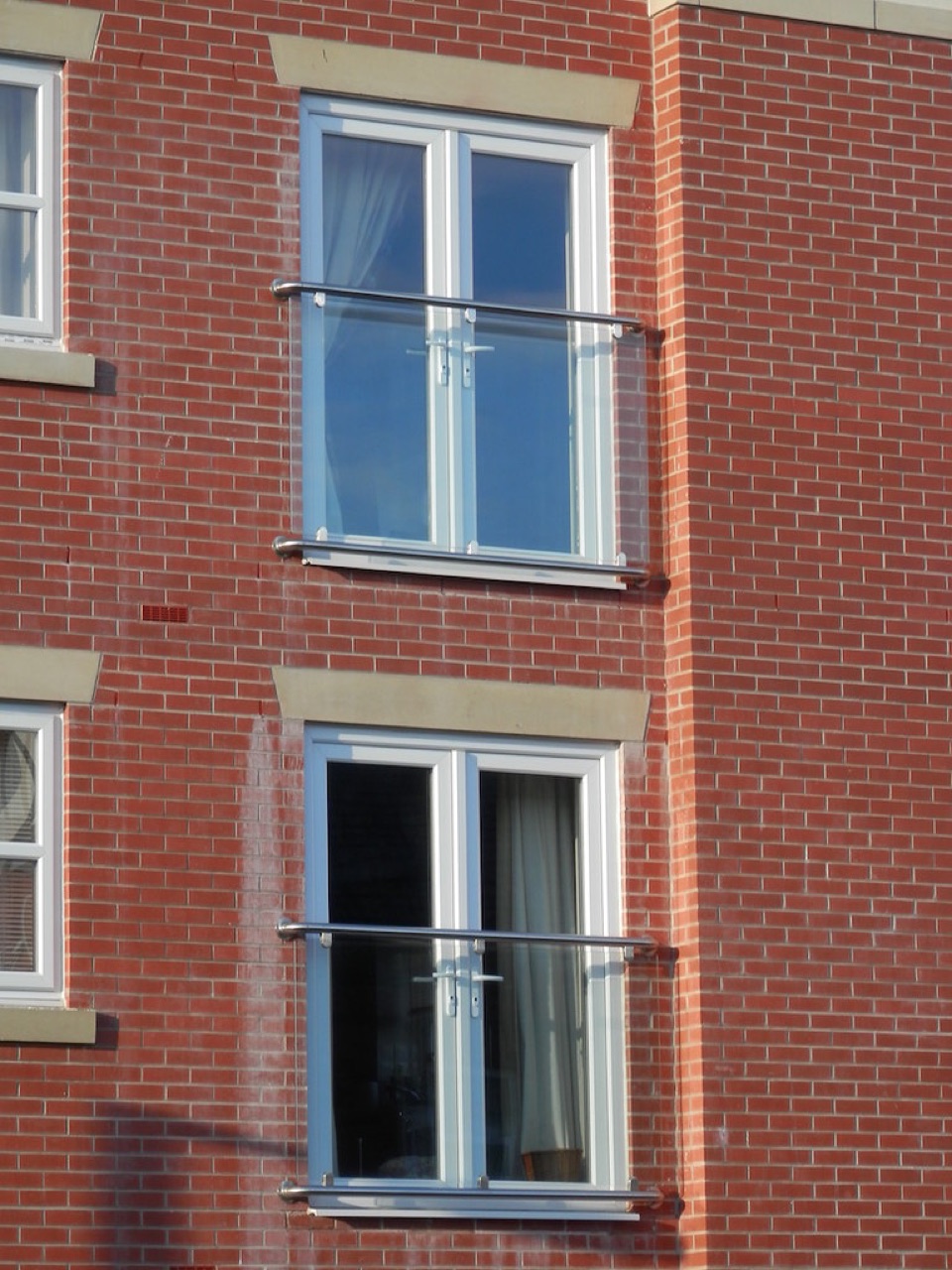 Juliet balconies with glass and steel balustrades on the brick face of a modern block of flats