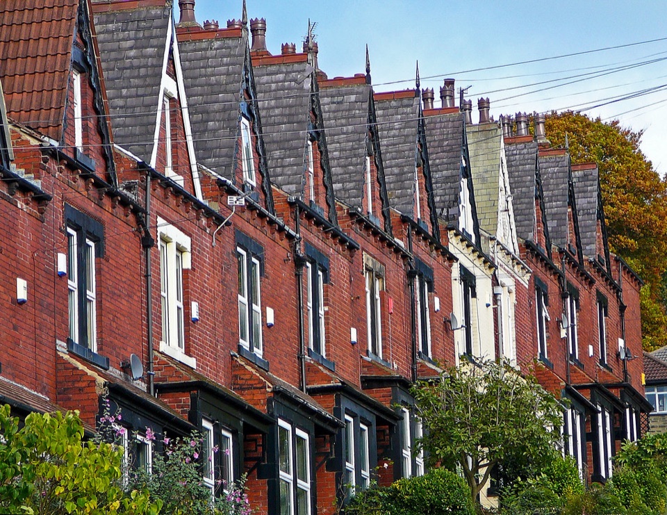 A row of red brick terraced houses with gabled slate roofs on a street in Leeds
